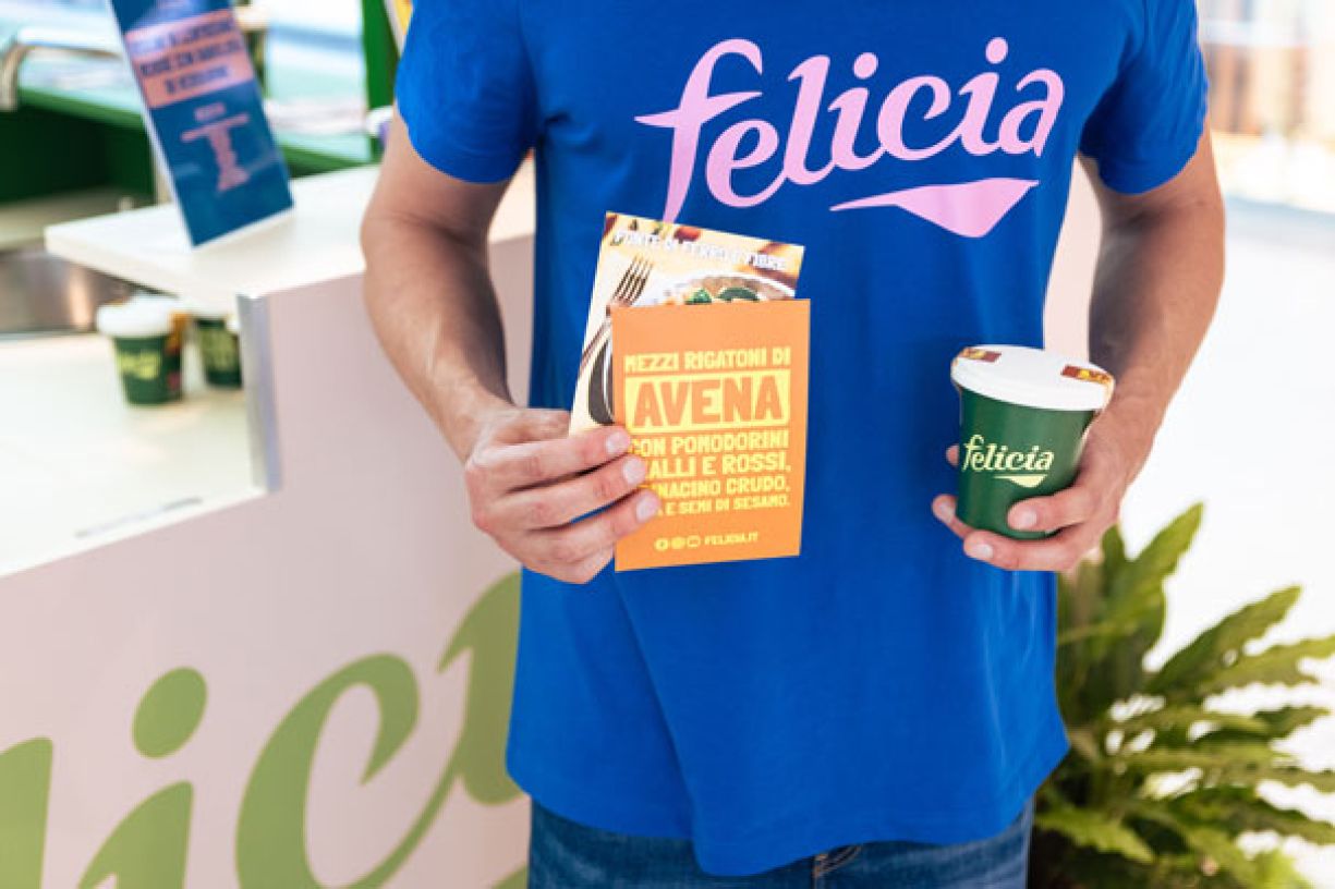 Staff con t-shirt blu con logo pasta Felicia mostra cartoline pubblicitarie  e contenitore degustazione con logo evento