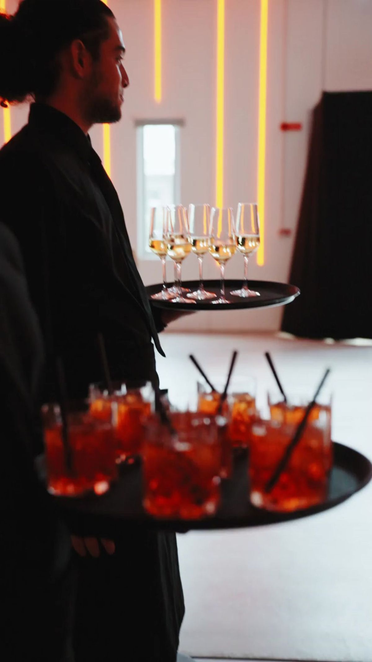 Due camerieri di Zeta Eventi offrono vassoi con calici di vino bianco e negroni agli ospiti di About Pharma Awards 2025