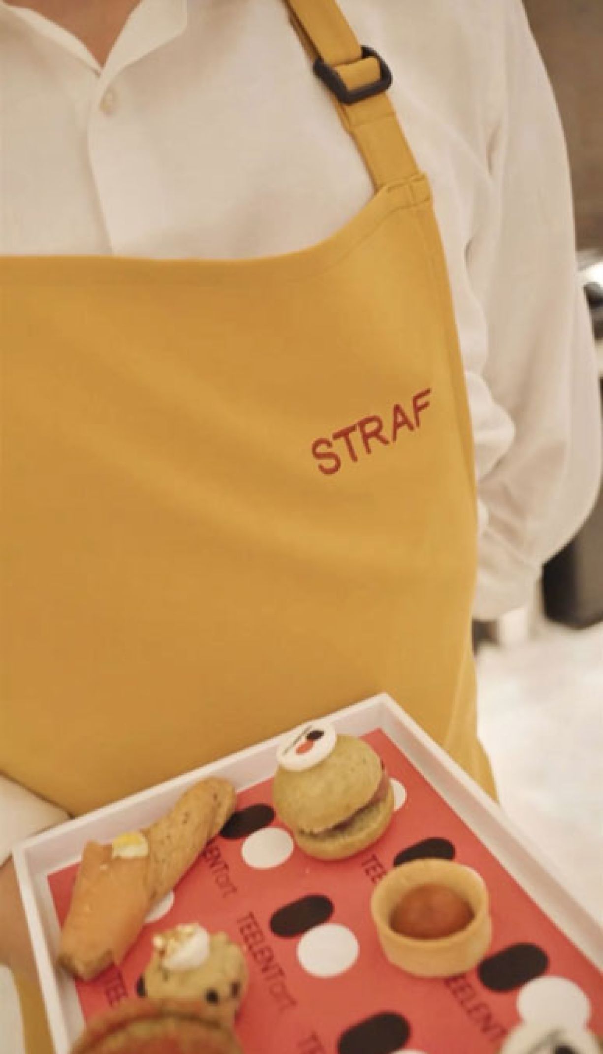 Cameriere con grembiule giallo logo Straf rosso e vassoio con tovaglietta logata evento serve l'aperitivo