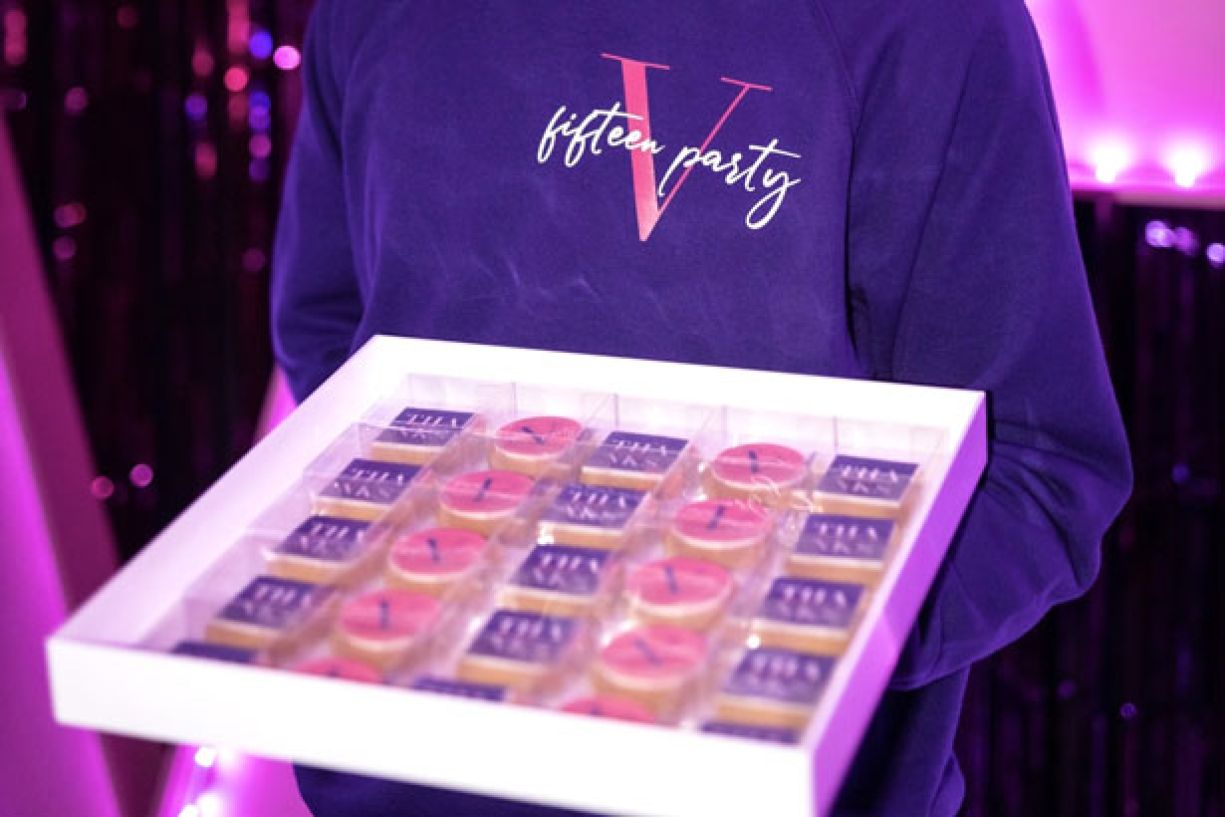 Cameriere con felpa viola e logo "V fifteen party" porta vassoio con biscotti con logo della festa