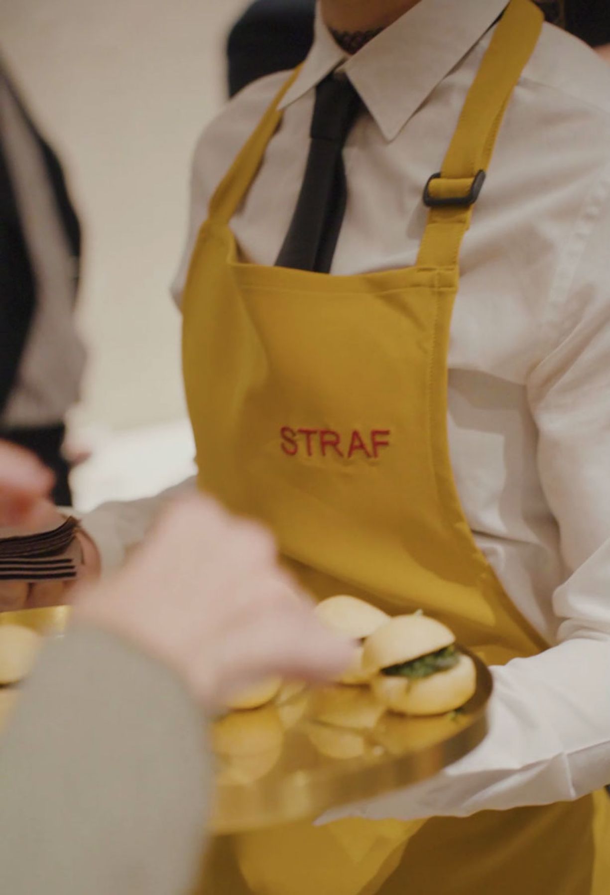 Cameriere con grembiule giallo logo rosso Straf serve vassoio di appetizer a un cocktail di Zeta Eventi Milano
