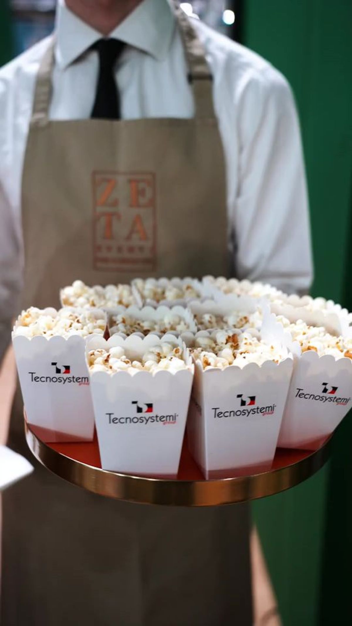 Cameriere con vassoio di pop corn in contenitori con logo azienda allo stand Tecnosystemi MCE 2024 Fiera Milano Rho